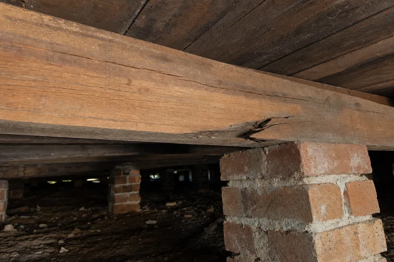 A split timber beam with a sag over a brick pier under a floor — subfloor repair, Melbourne. Illustrative example.